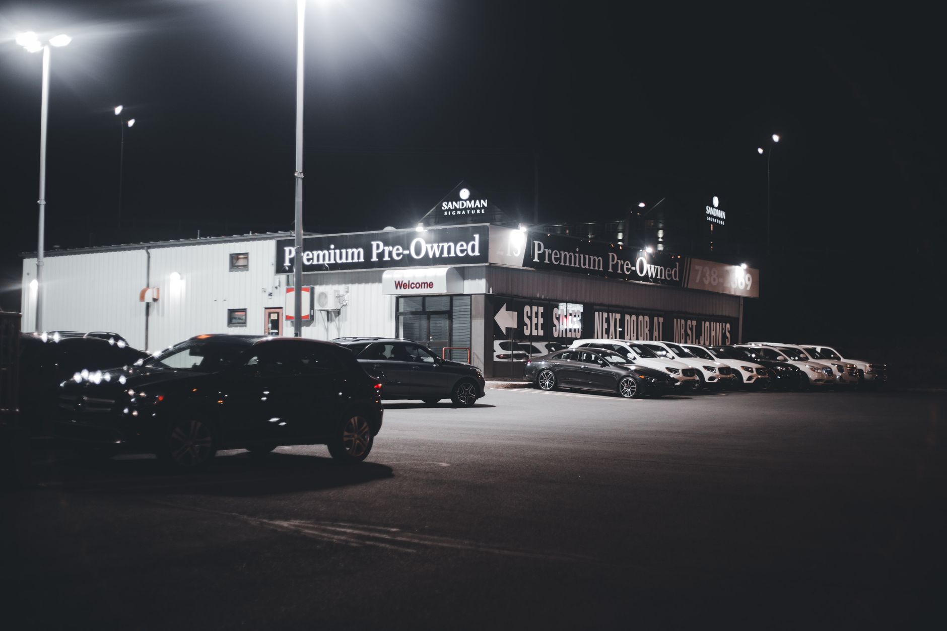 Rows of pre-owned cars on a lit dealership lot at night
