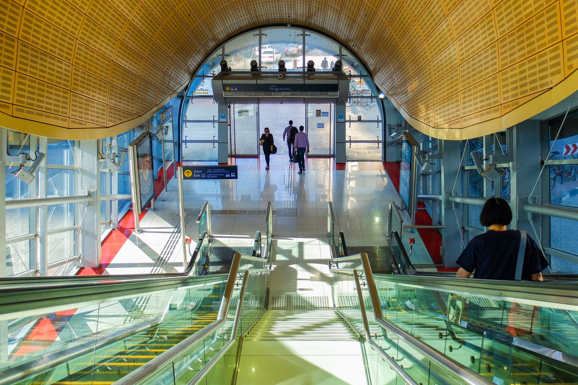 Commuters on escalators inside a sunlit Dubai Metro station